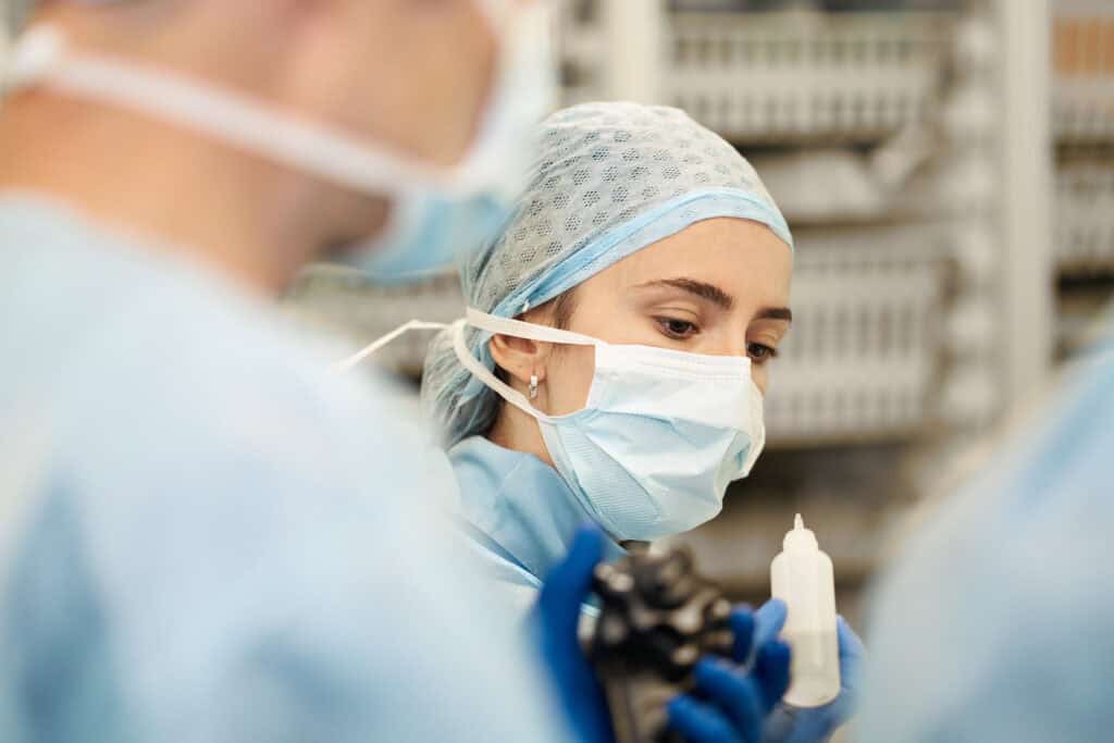 Medizinisches Team in Operationssaal trägt Schutzmasken und OP-Kleidung, arbeitet sorgfältig an einem medizinischen Eingriff, um höchste Hygiene und Sicherheit zu gewährleisten.