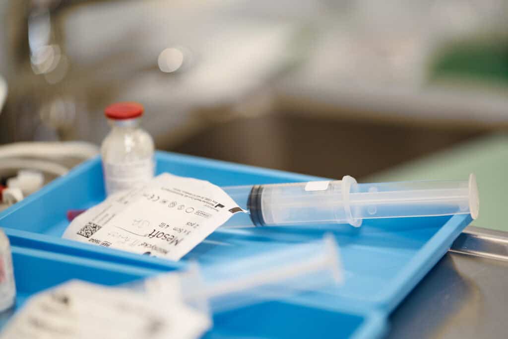 Medizinische Geräte und Medikamente, inklusive Spritze und Ampullen, auf einem blauen medizinischen Tablett, bereit für die Anwendung in einer Klinik oder Praxis.