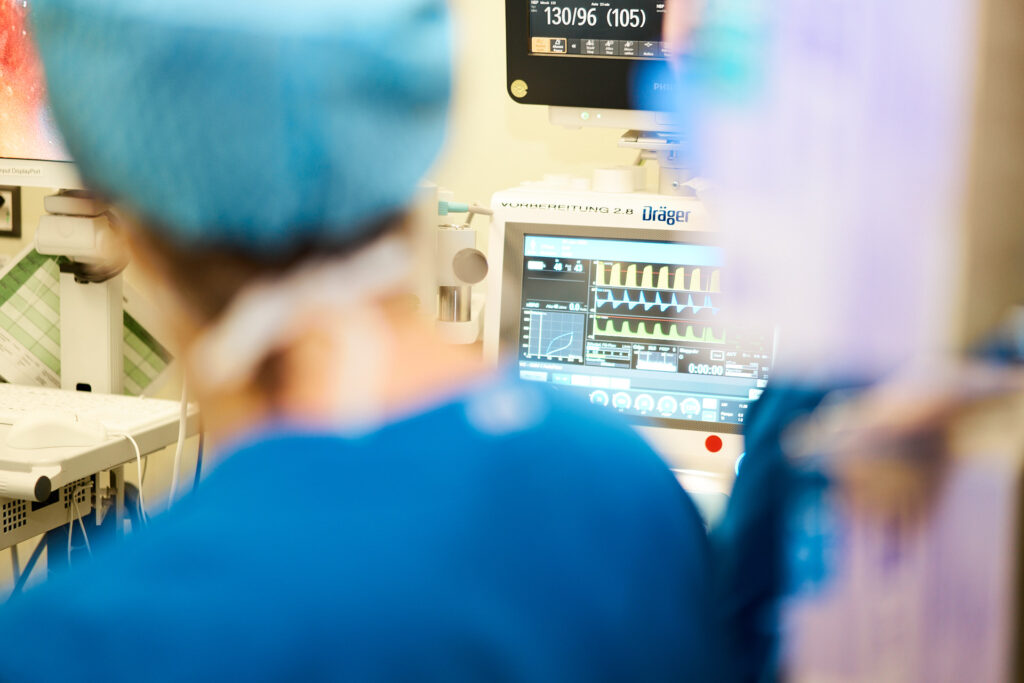 Medizinisches Personal überwacht Vitalparameter auf einem Monitor im Operationssaal, um die Gesundheit der Patienten während der Operation sicherzustellen.