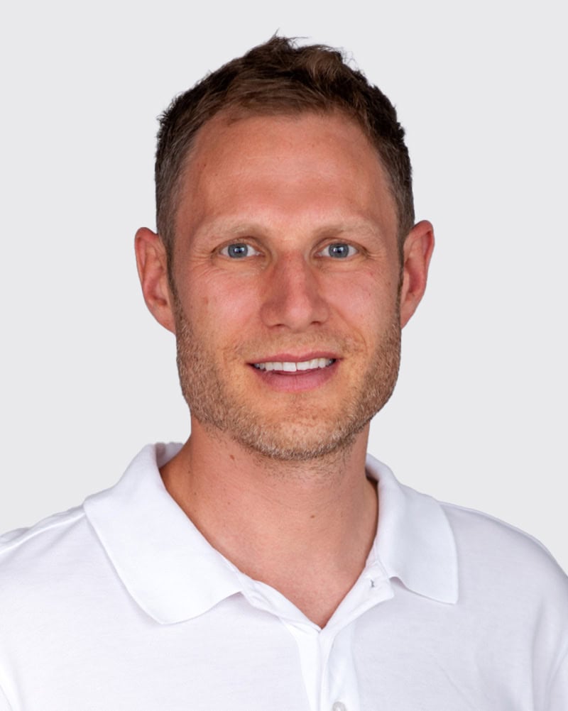 Mann in weißem Polo-Shirt, lächelnd, professionell, auf hellem Hintergrund.